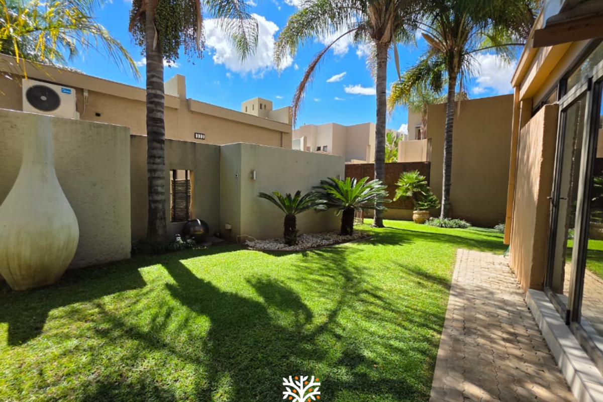A well-maintained rear garden featuring a lush lawn, paved walkway, and established palm trees, providing a private outdoor space.