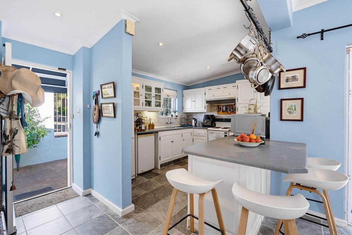A functional kitchen featuring white cabinetry, a central island with breakfast bar seating, and tiled flooring, with direct access to an outdoor patio area.