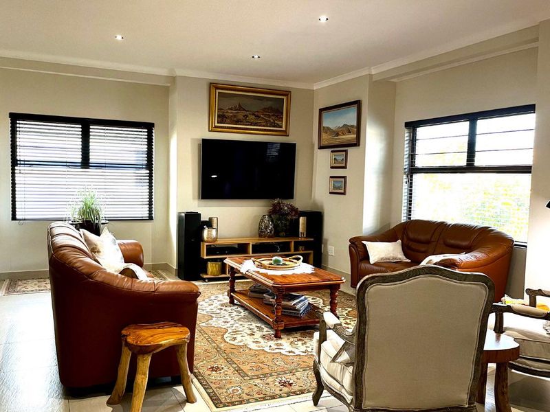 A well-maintained living room featuring neutral tiled flooring, recessed downlighting, and large windows fitted with venetian blinds.