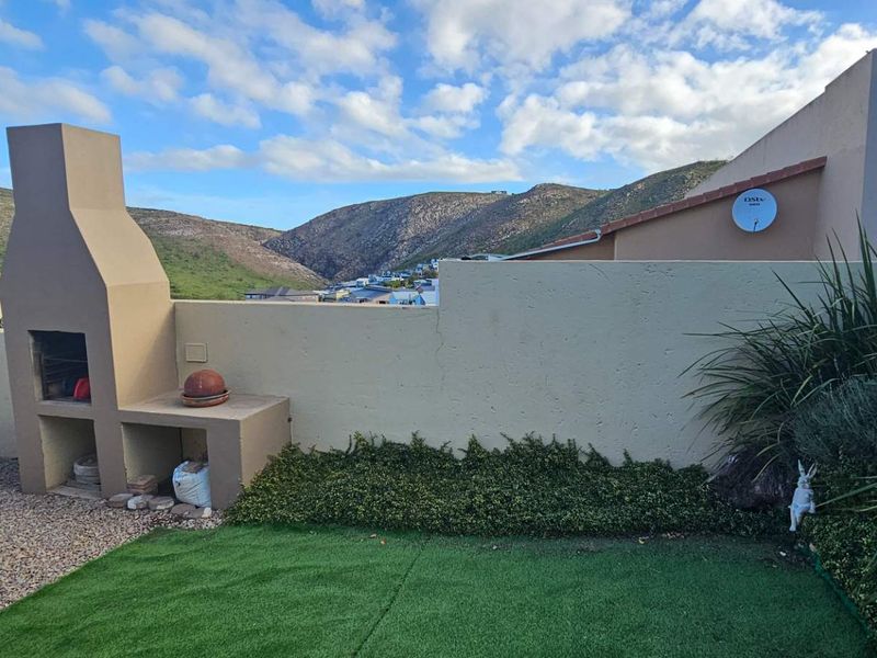 Rear garden area featuring a built-in braai, artificial lawn, and boundary wall with scenic mountain views.