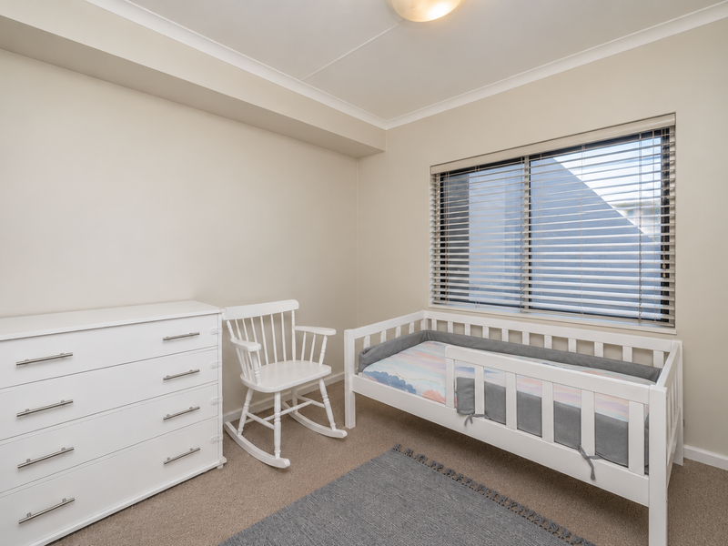 A well-maintained bedroom featuring neutral wall tones, carpeted flooring, and a window fitted with venetian blinds.