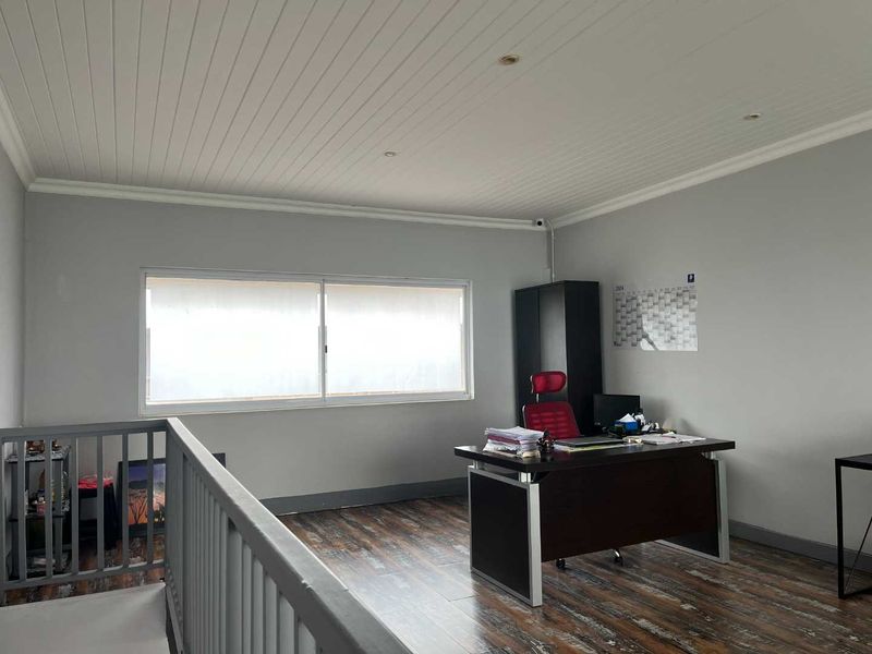 A functional office space featuring timber-look laminate flooring, a tongue and groove timber ceiling, and a balustrade overlooking the lower level.