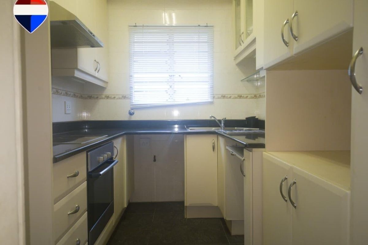 A compact, functional kitchen featuring built-in cabinetry, granite countertops, an integrated oven, extractor fan, and tiled finishes throughout.