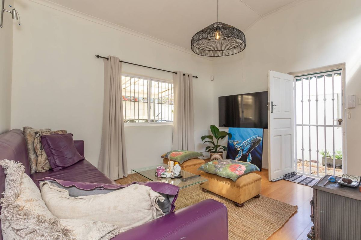 A bright living room featuring laminate flooring, a security gate at the entrance, and security bars on the windows.
