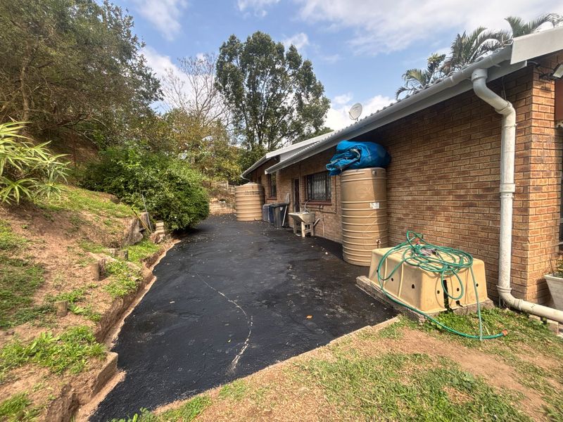 Rear exterior view of the property featuring brick walls, asphalt paving, and multiple rainwater storage tanks along the side of the house.