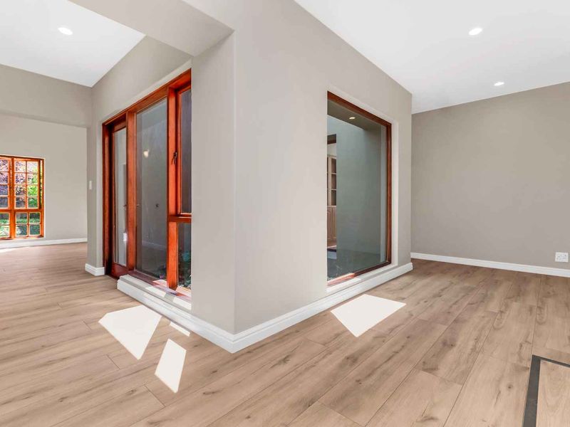 A bright, vacant living area featuring modern laminate flooring, recessed downlights, and large timber-framed windows and sliding doors providing natural light.