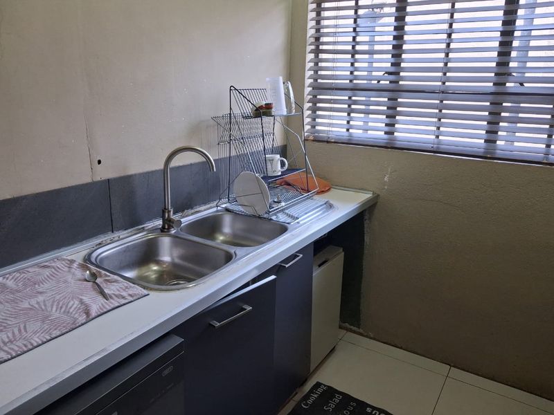 A functional scullery area featuring a double bowl stainless steel sink, tiled splashback, and base cabinetry with window blinds.