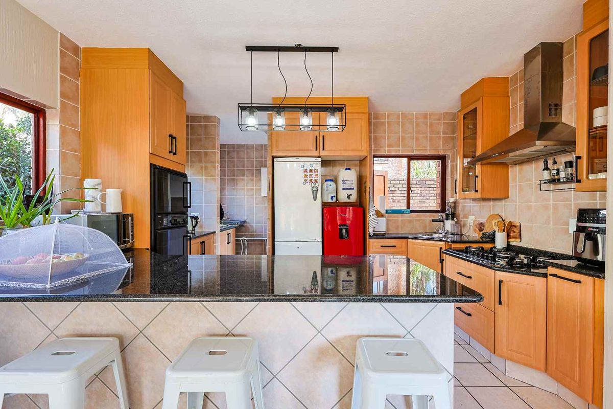 A functional kitchen featuring wooden cabinetry, granite countertops, a central island, and a gas hob with a stainless steel extractor fan.