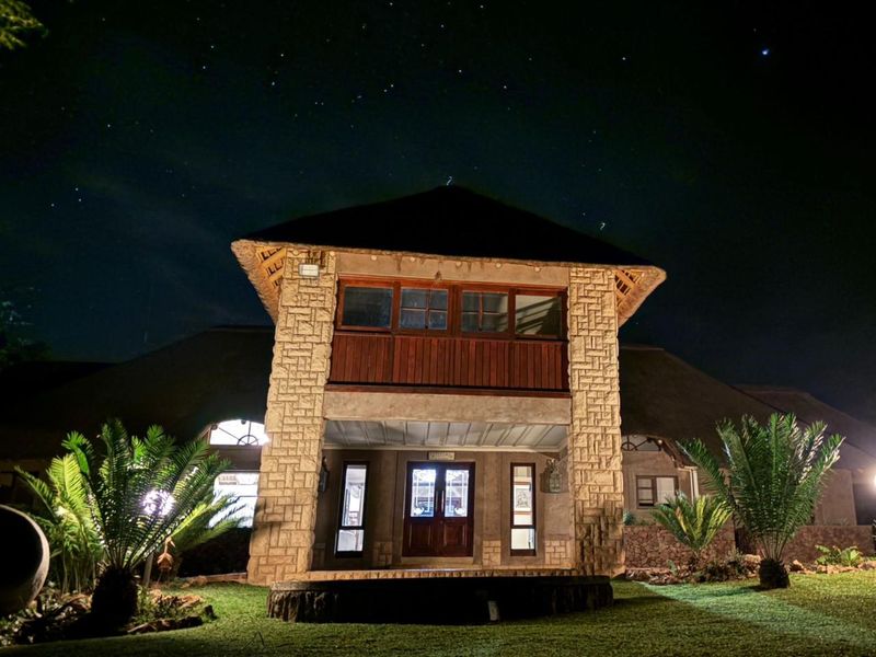 A night view of the property featuring a distinctive thatched roof, stone facade, and a timber balcony above the main entrance.