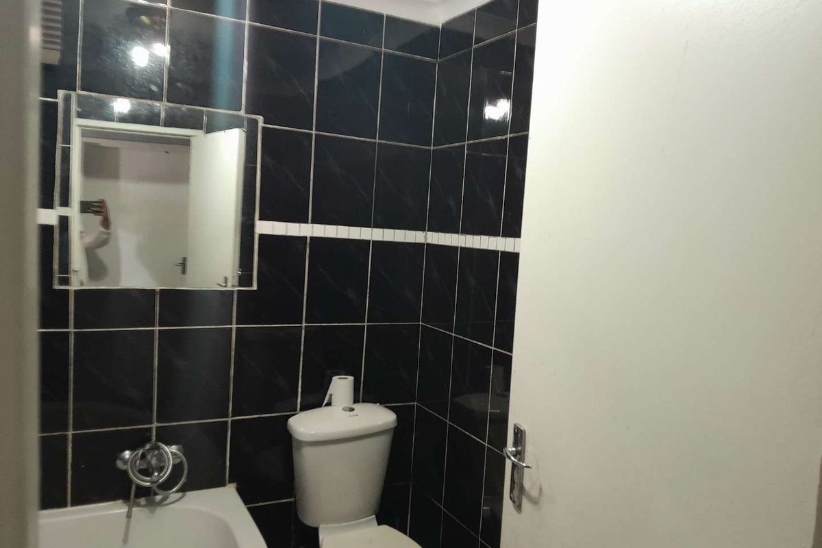 A compact bathroom featuring dark wall tiling, a standard white toilet, and a built-in bathtub with chrome fixtures.