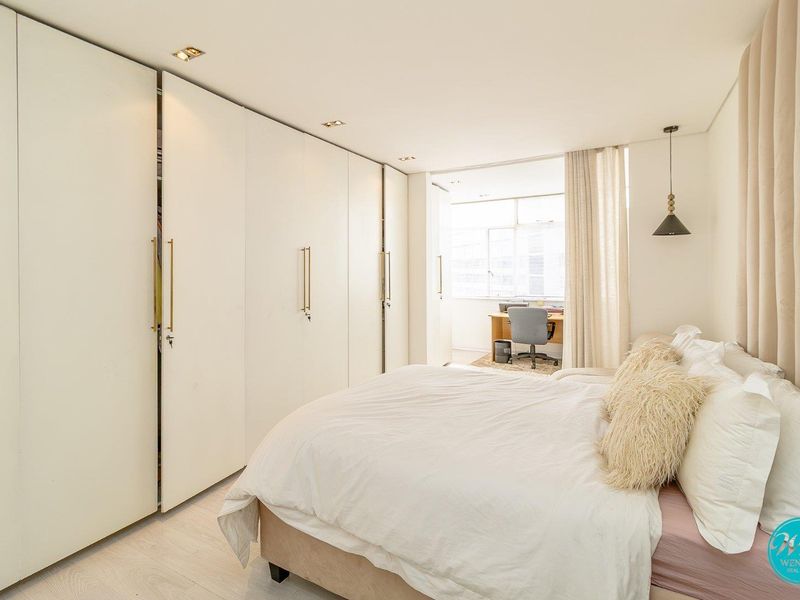 A bright and modern bedroom featuring extensive floor-to-ceiling built-in cupboards, recessed lighting, and light-toned laminate flooring.