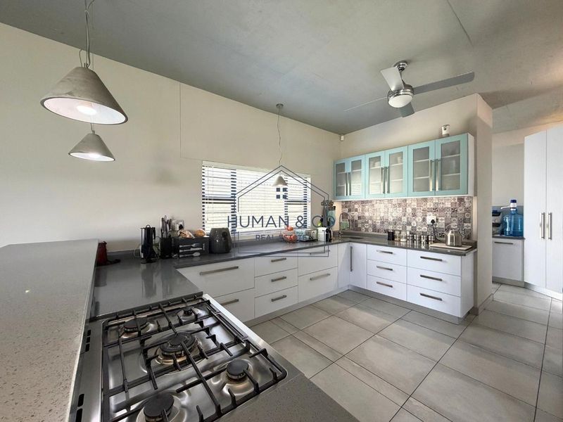 Modern kitchen featuring white cabinetry, quartz countertops, a gas hob, patterned tile backsplash, and stylish pendant lighting.