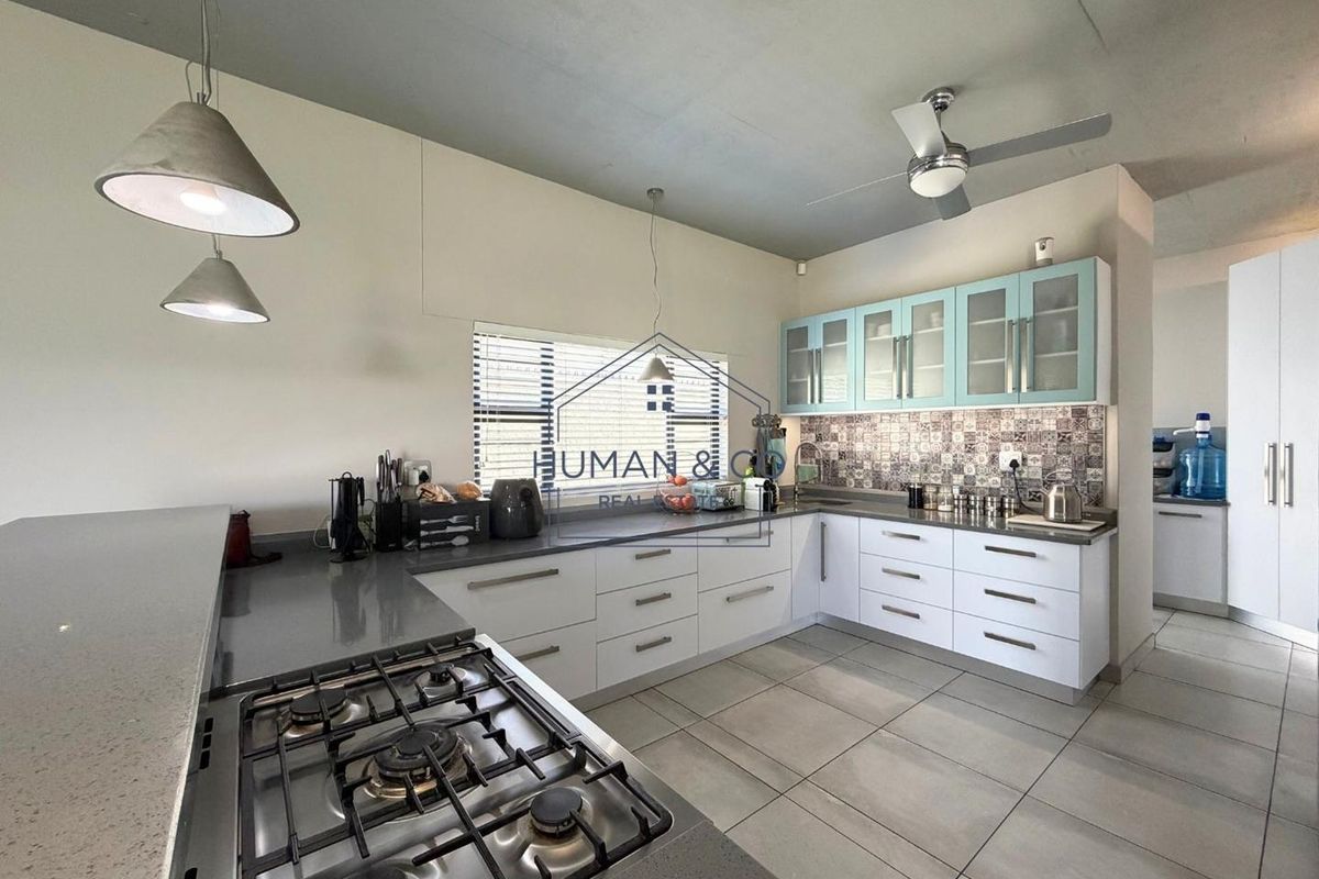 Modern kitchen featuring white cabinetry, quartz countertops, a gas hob, patterned tile backsplash, and stylish pendant lighting.