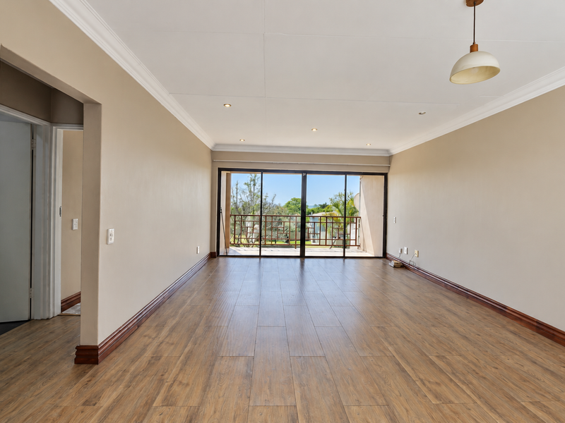 A spacious, empty living room featuring wood-look laminate flooring, recessed lighting, and large sliding glass doors that open onto a balcony.