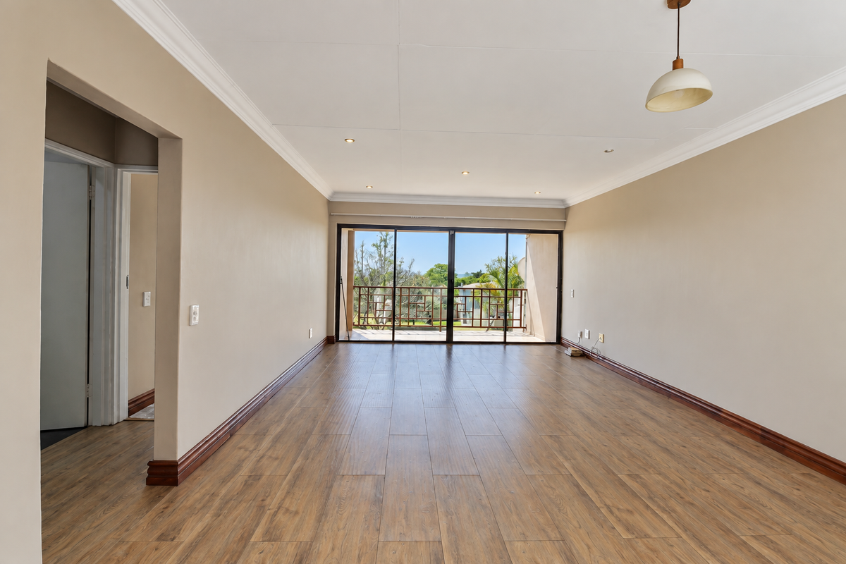 A spacious, empty living room featuring wood-look laminate flooring, recessed lighting, and large sliding glass doors that open onto a balcony.