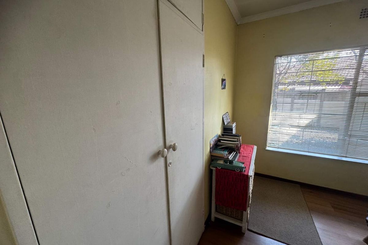 A bedroom featuring built-in cupboards, laminate flooring, and a window with horizontal blinds, offering a functional space with potential for cosmetic updates.