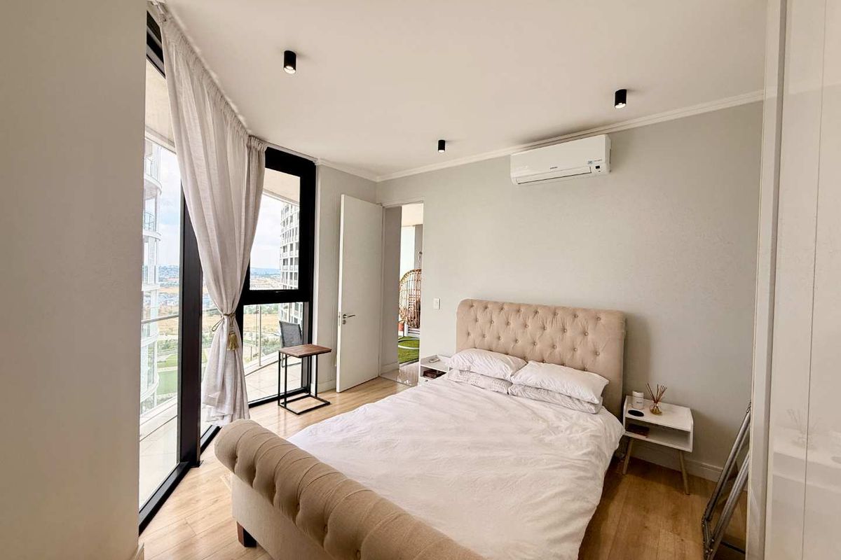 A bright, modern bedroom featuring laminate flooring, recessed lighting, a split-system air conditioner, and floor-to-ceiling windows offering expansive views.