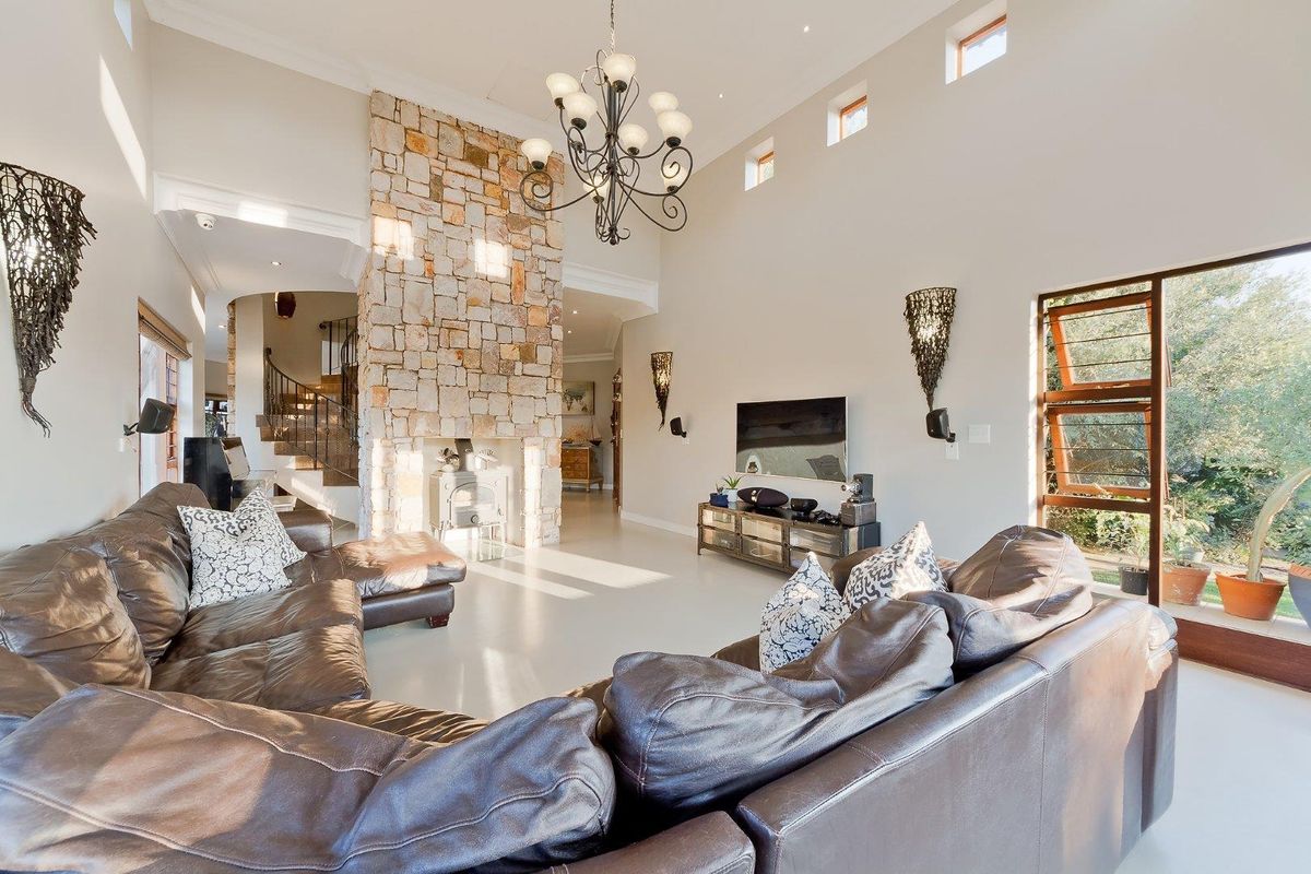 Spacious living room featuring a double-volume ceiling, a striking stone-clad fireplace, and large windows that provide ample natural light.