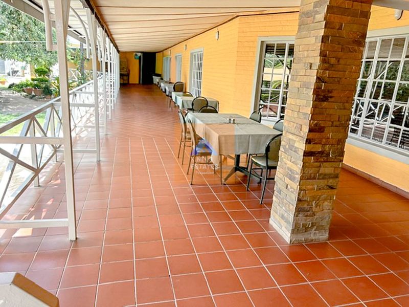 A spacious covered patio area featuring terracotta tiled flooring, a stone-clad support pillar, and a metal railing overlooking the garden.