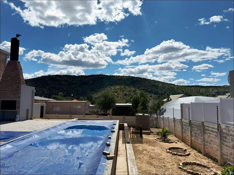 Outdoor pool area featuring a built-in braai, covered swimming pool, and mountain views, enclosed by precast walling with electric fencing.