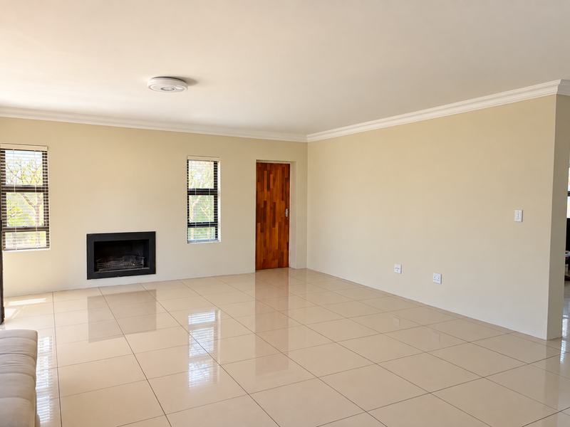Spacious, empty living room featuring large neutral floor tiles, a built-in fireplace, and a wooden door, offering a clean and well-maintained blank canvas.