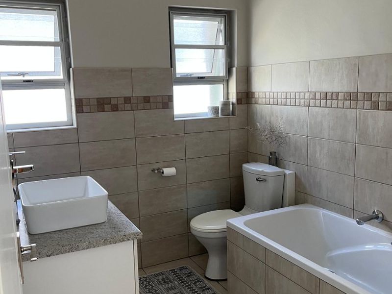 A well-maintained bathroom featuring a vessel sink on a granite vanity, a bathtub, and neutral wall and floor tiling.