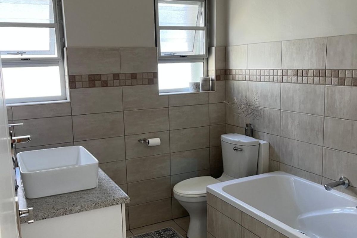 A well-maintained bathroom featuring a vessel sink on a granite vanity, a bathtub, and neutral wall and floor tiling.