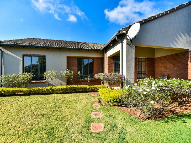 A well-maintained townhouse rear elevation featuring a covered patio, brick and plaster facade, tiled roof, and a landscaped garden with a stone pathway.