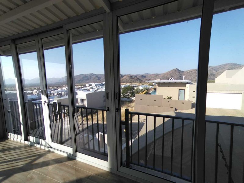 A covered balcony featuring modern aluminium sliding doors, tiled flooring, and a metal balustrade, offering expansive views of the surrounding landscape.