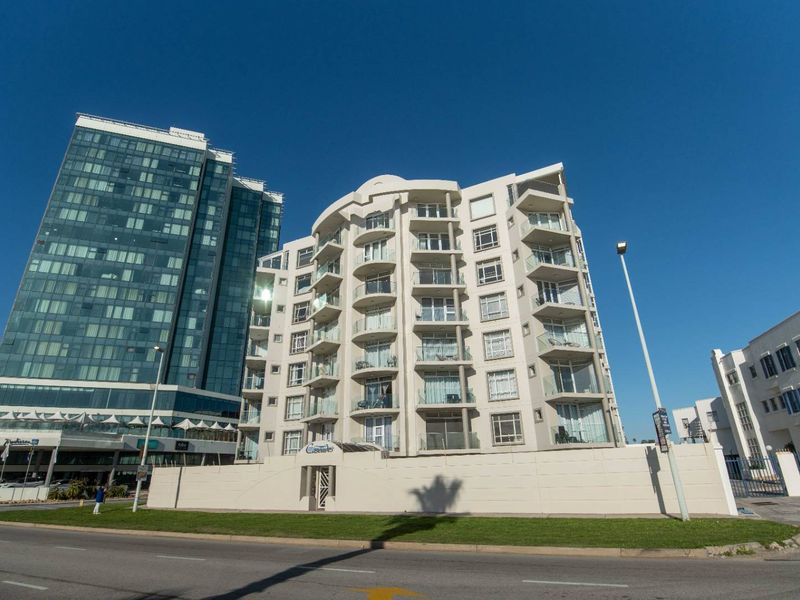 Exterior view of a multi-story apartment building featuring private balconies with glass balustrades and a secure perimeter wall.