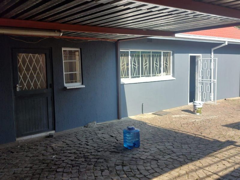 Rear exterior view featuring a covered carport area, cobblestone paving, and secure access points with metal security gates and window bars.