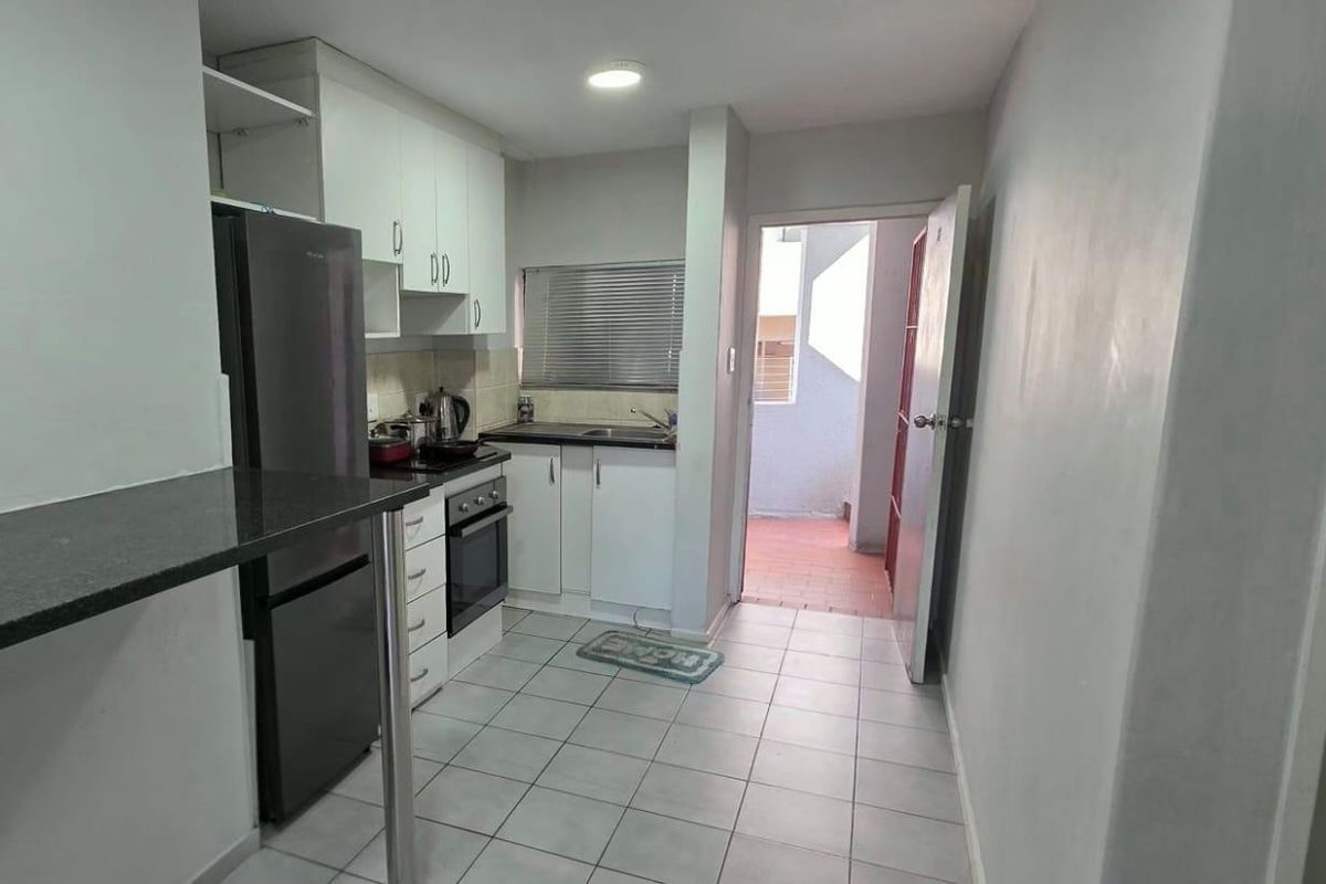 Compact kitchen featuring white built-in cabinetry, granite countertops, a built-in oven and hob, and tiled flooring with direct access to an outdoor area.
