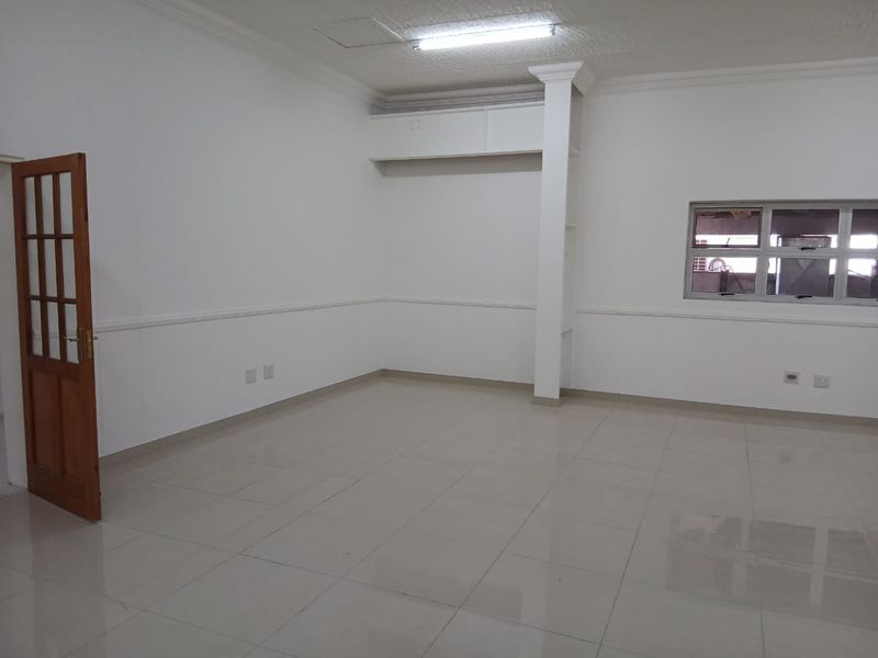 A clean, vacant office space featuring tiled flooring, built-in storage cabinetry, and neutral white walls, suitable for a professional workspace.