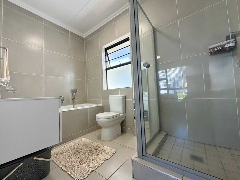 Modern bathroom featuring a built-in bathtub, a separate glass-enclosed shower, and neutral floor-to-ceiling tiling.