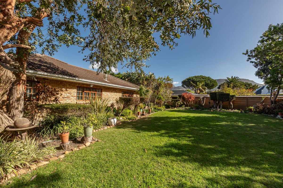 A well-maintained rear garden featuring a lush lawn, established trees, and a brick-faced exterior wall of the house.