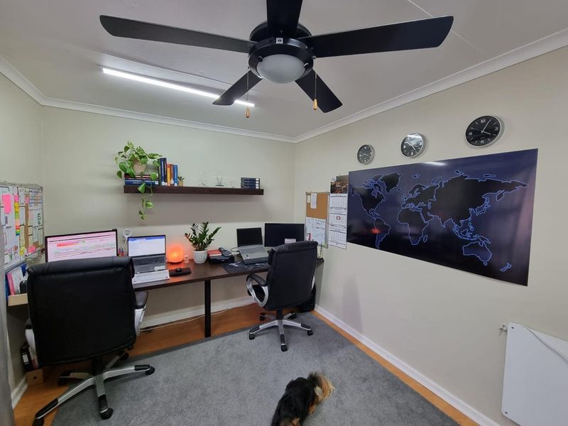 A functional home office space featuring a ceiling fan, floating shelving, and neutral wall finishes, suitable for a dedicated workspace.
