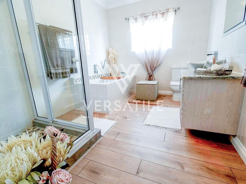 A well-maintained bathroom featuring a glass-enclosed shower, a built-in bathtub, a vanity cabinet, and modern wood-look tiled flooring.