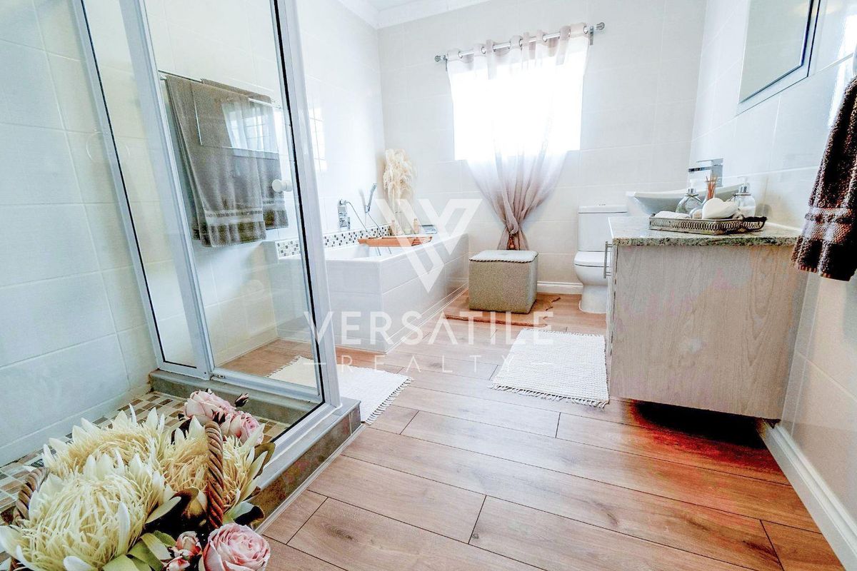A well-maintained bathroom featuring a glass-enclosed shower, a built-in bathtub, a vanity cabinet, and modern wood-look tiled flooring.