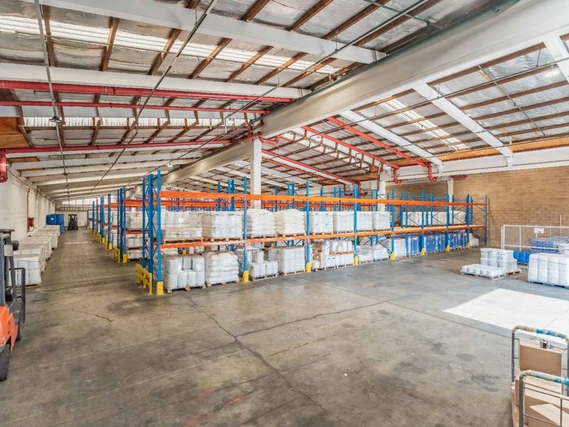 Spacious industrial warehouse featuring high ceilings with exposed steel trusses, fire sprinkler systems, and extensive built-in racking for storage.