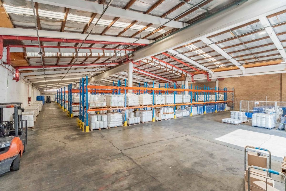 Spacious industrial warehouse featuring high ceilings with exposed steel trusses, fire sprinkler systems, and extensive built-in racking for storage.