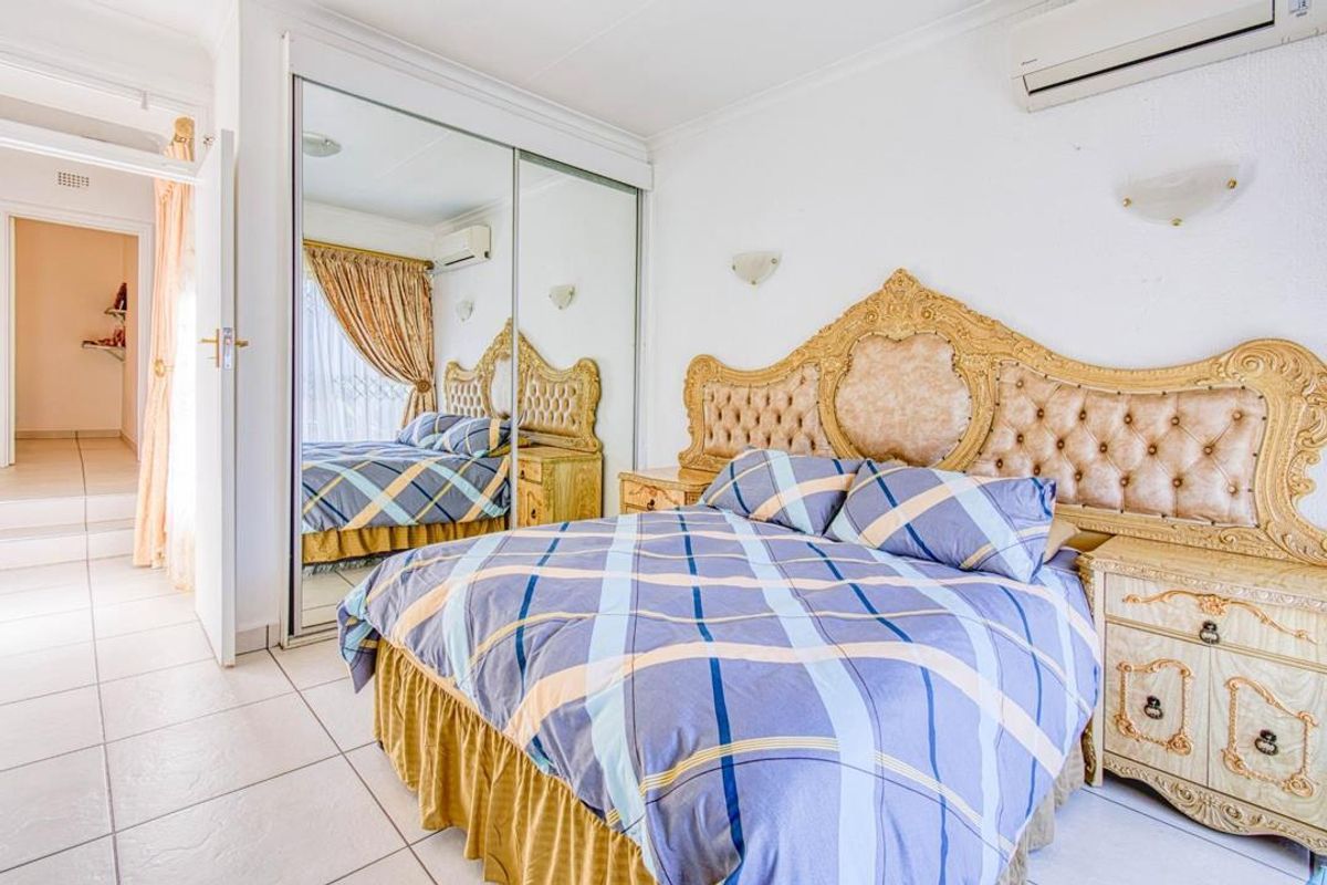 A bedroom featuring tiled flooring, built-in mirrored sliding wardrobes, and a wall-mounted air conditioning unit.