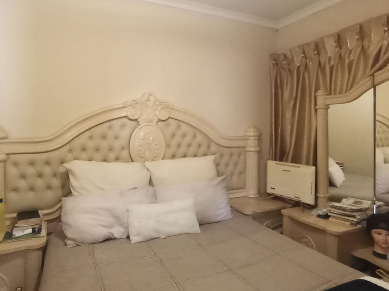 A bedroom featuring a large, ornate built-in headboard and matching integrated bedside tables, providing a classic aesthetic foundation for the space.