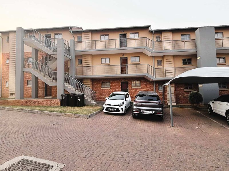 Exterior view of a multi-story apartment complex featuring brick paving, covered parking bays, and external staircases providing access to upper-level units.