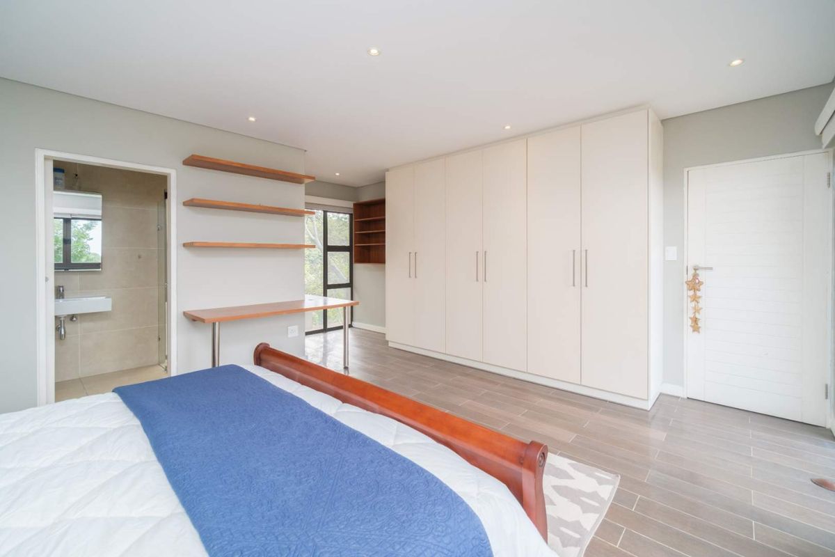 Spacious bedroom featuring built-in floor-to-ceiling wardrobes, a custom floating desk with shelving, and an en-suite bathroom with modern finishes.
