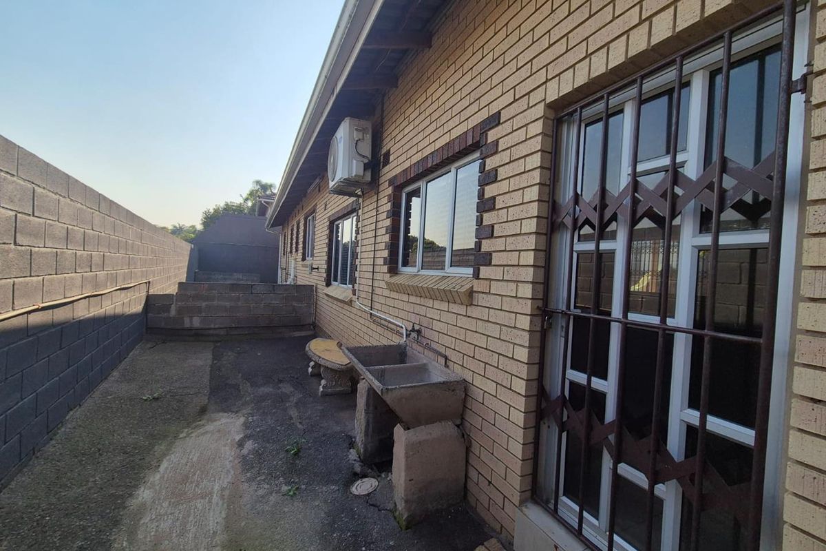 Rear exterior view of the property featuring a brick facade, security gate, and a concrete utility sink area along the side path.