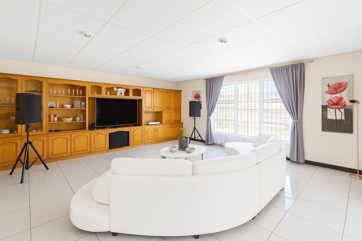 Spacious living room featuring large format floor tiles, a built-in wooden cabinetry wall unit, and expansive windows with security bars.