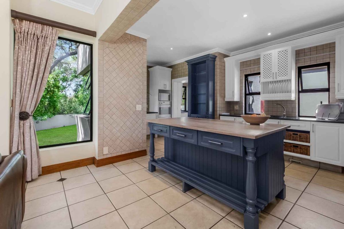 A well-appointed kitchen featuring a central island, custom cabinetry, tiled flooring, and large windows providing natural light and garden views.