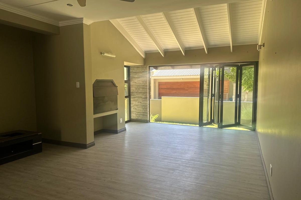Spacious living area featuring vaulted ceilings, a built-in fireplace, and large folding glass doors that open to the outdoor patio area.
