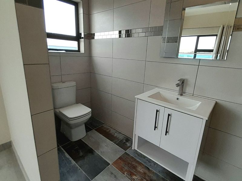 A modern, clean bathroom featuring neutral wall tiles, a vanity with basin, and a toilet.
