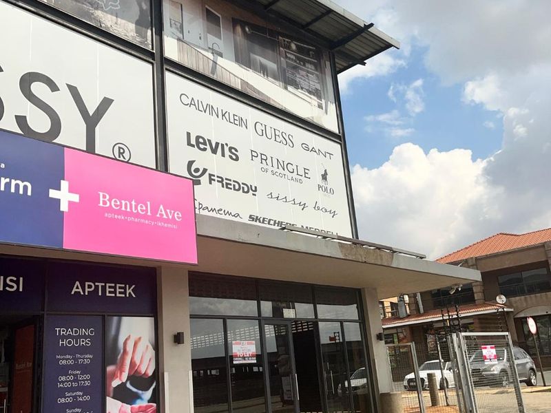 Front elevation of a retail commercial property featuring large glass storefront windows, metal awning, and prominent signage space in a well-maintained shopping center.